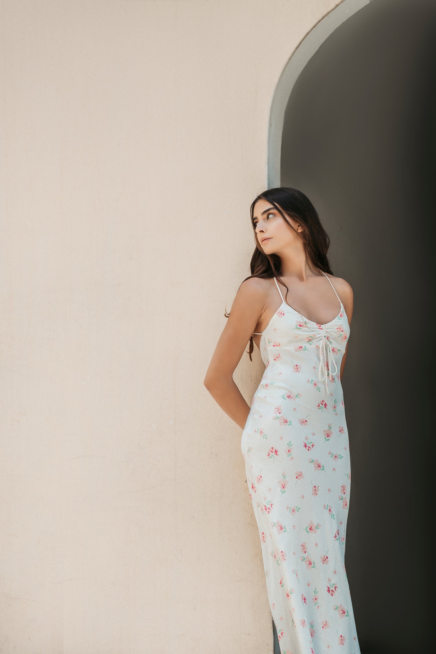 rosafa model in a white floral dress leaning against a wall